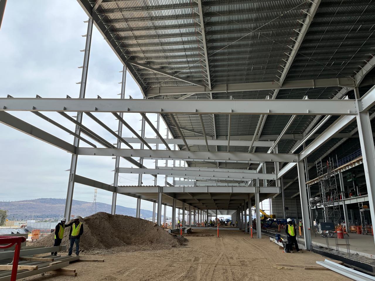Interior de nave industrial con estructura de acero y trabajadores en obra